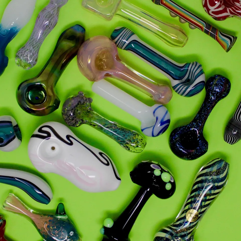 Colorful hand-blown glass spoon pipes scattered on a lime green backdrop