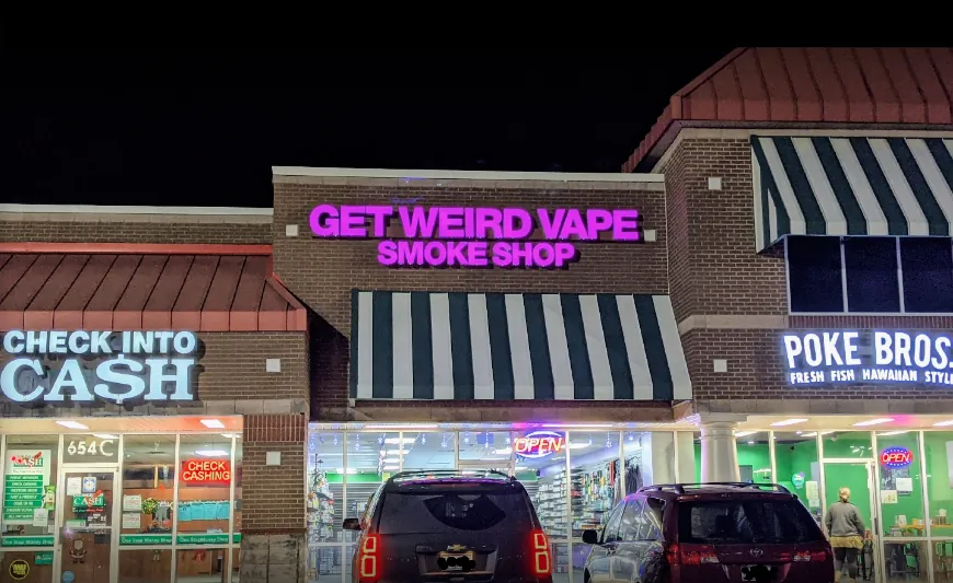 Get Weird Vape Smoke Shop sign glowing purple in the Fairview Road shopping center at night
