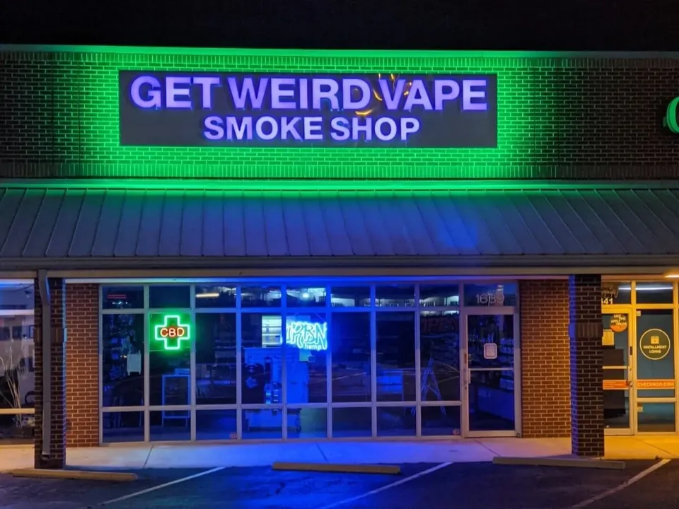 Get Weird Vape Smoke Shop storefront on Woodruff Road lit up in green neon at night